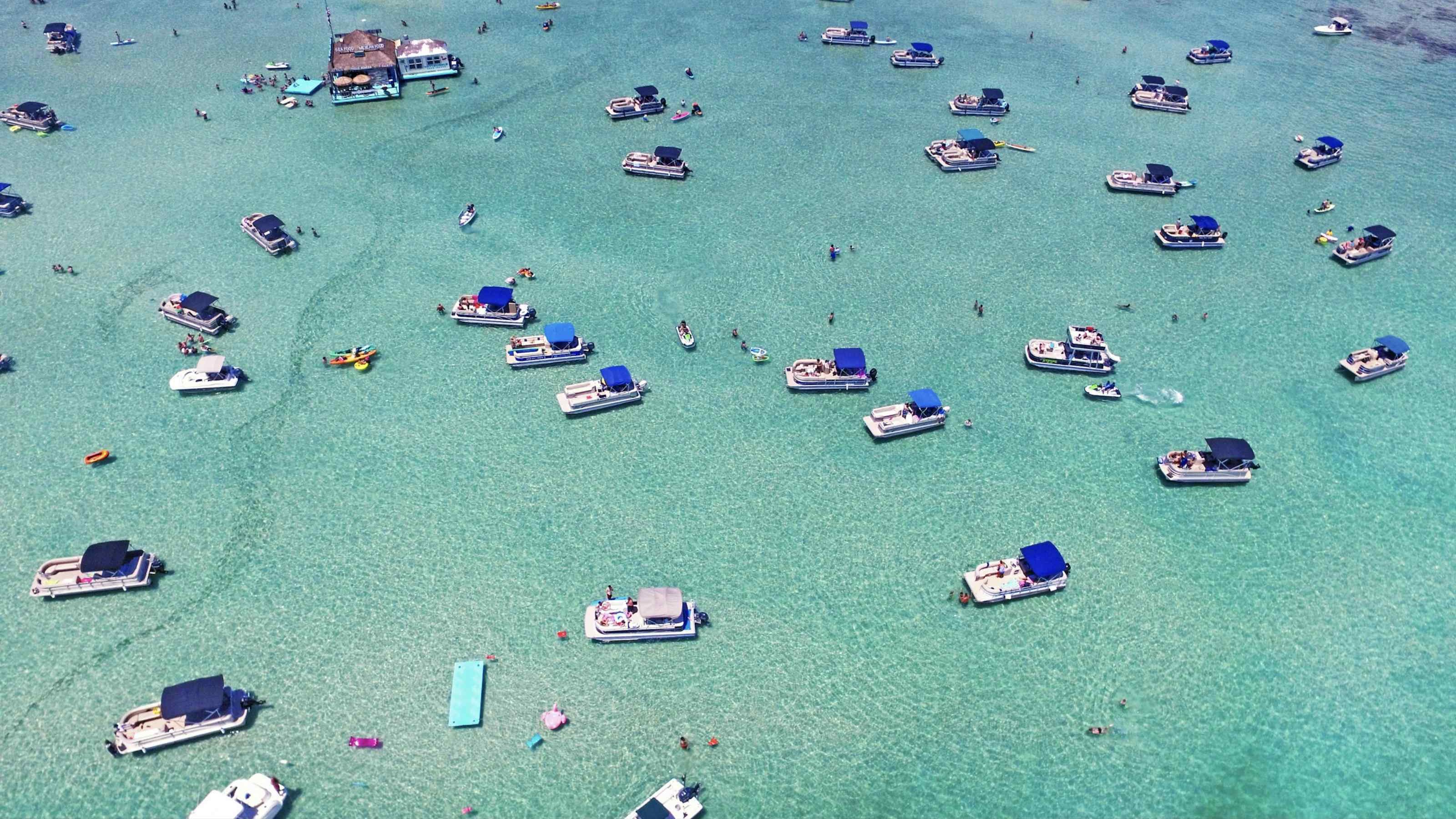 Pontoon boats anchored at Crab Island in clear emerald water